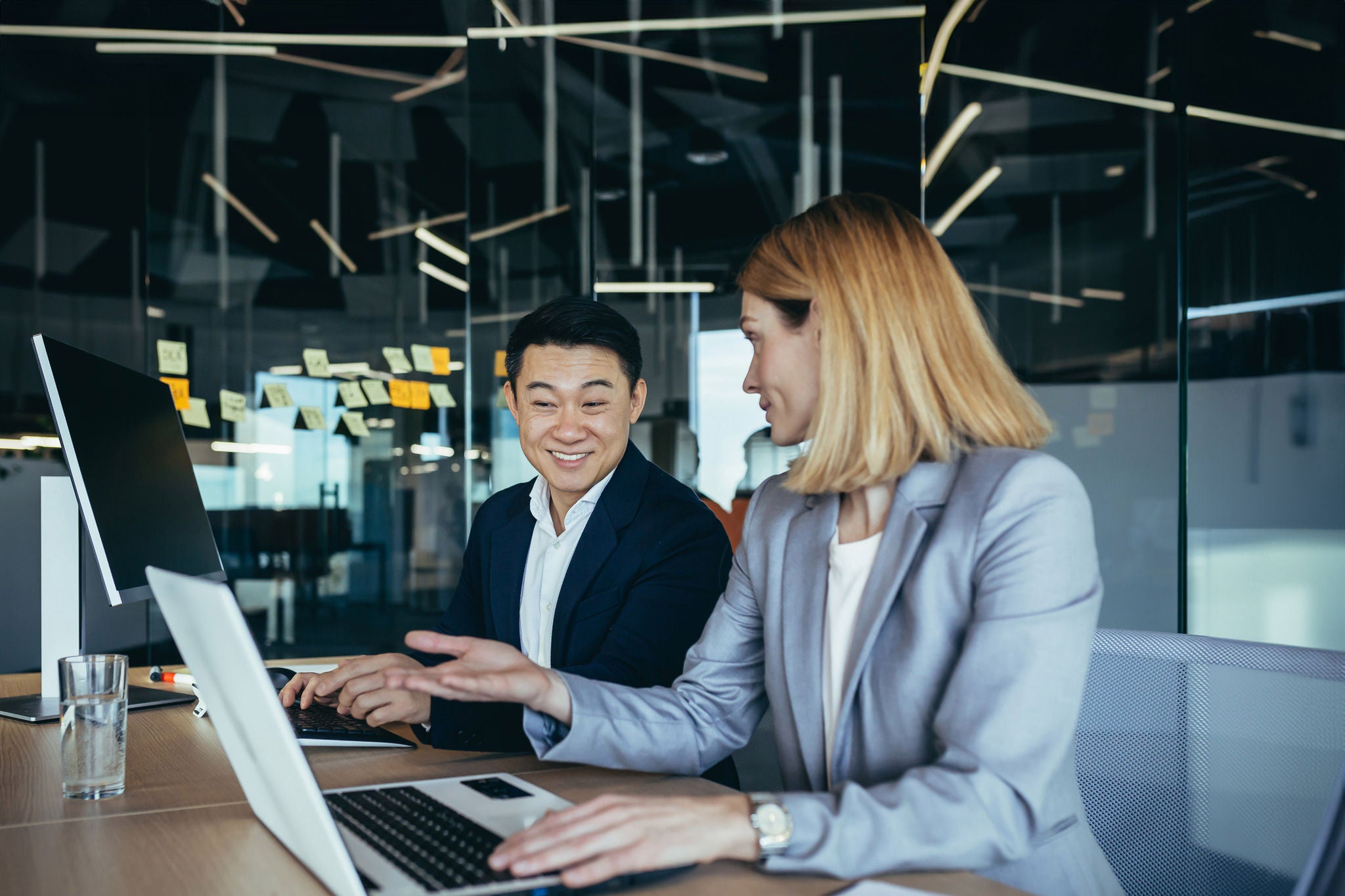 happy coworkers discuss project strategy by looking and pointing at laptop pc computer monitor screen. multiethnic business team in the office. confident mature asian man explaining young female