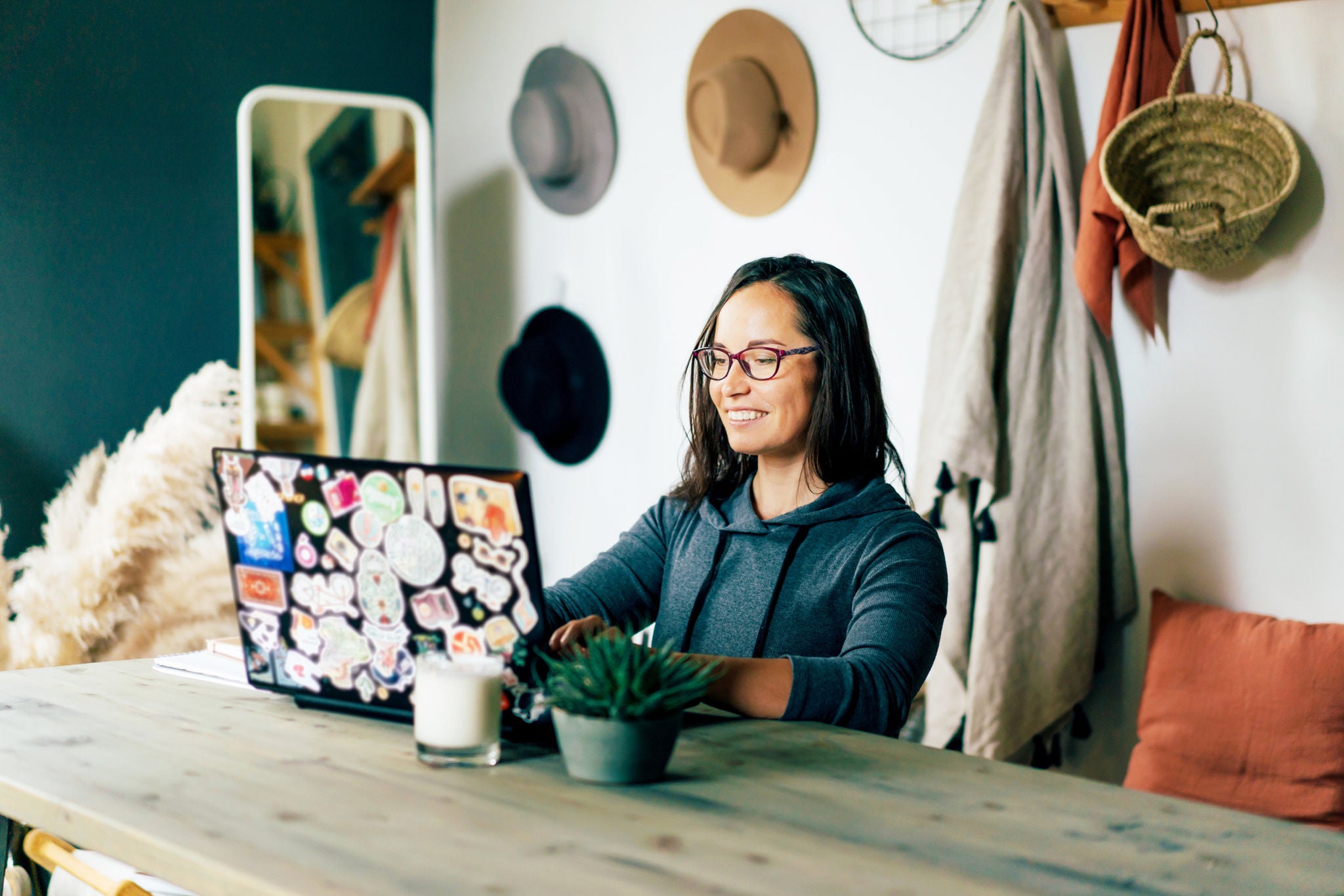 Happy brunette woman works on a laptop decorated with pictures in the interior of a cozy living room of her apartment. Remote work from home. Online trainings and professional development.