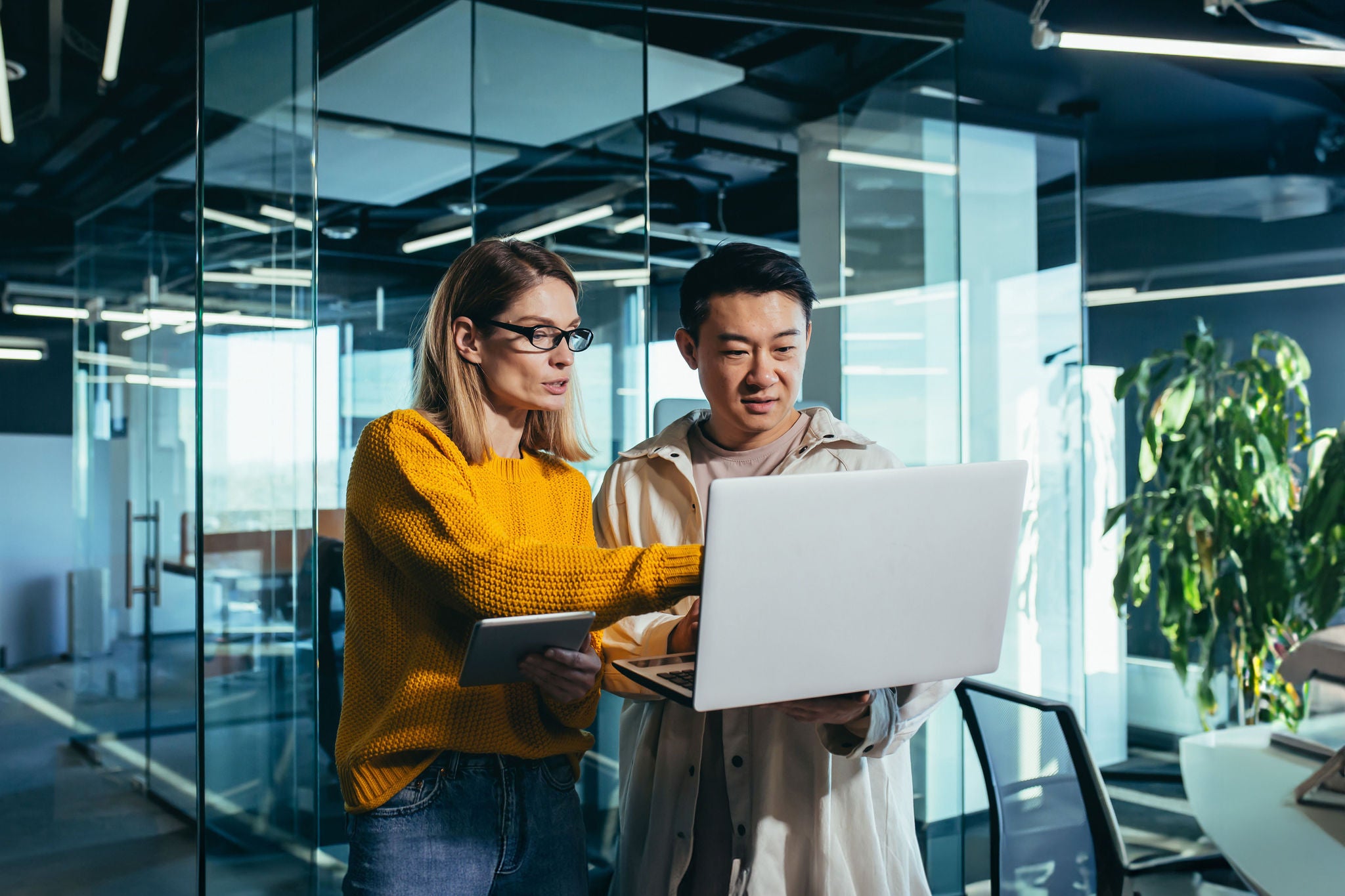 Business meeting of two employees, Asian and female colleagues, discussing the project, working in a modern office, looking at a laptop screen, discussing edits, and project success