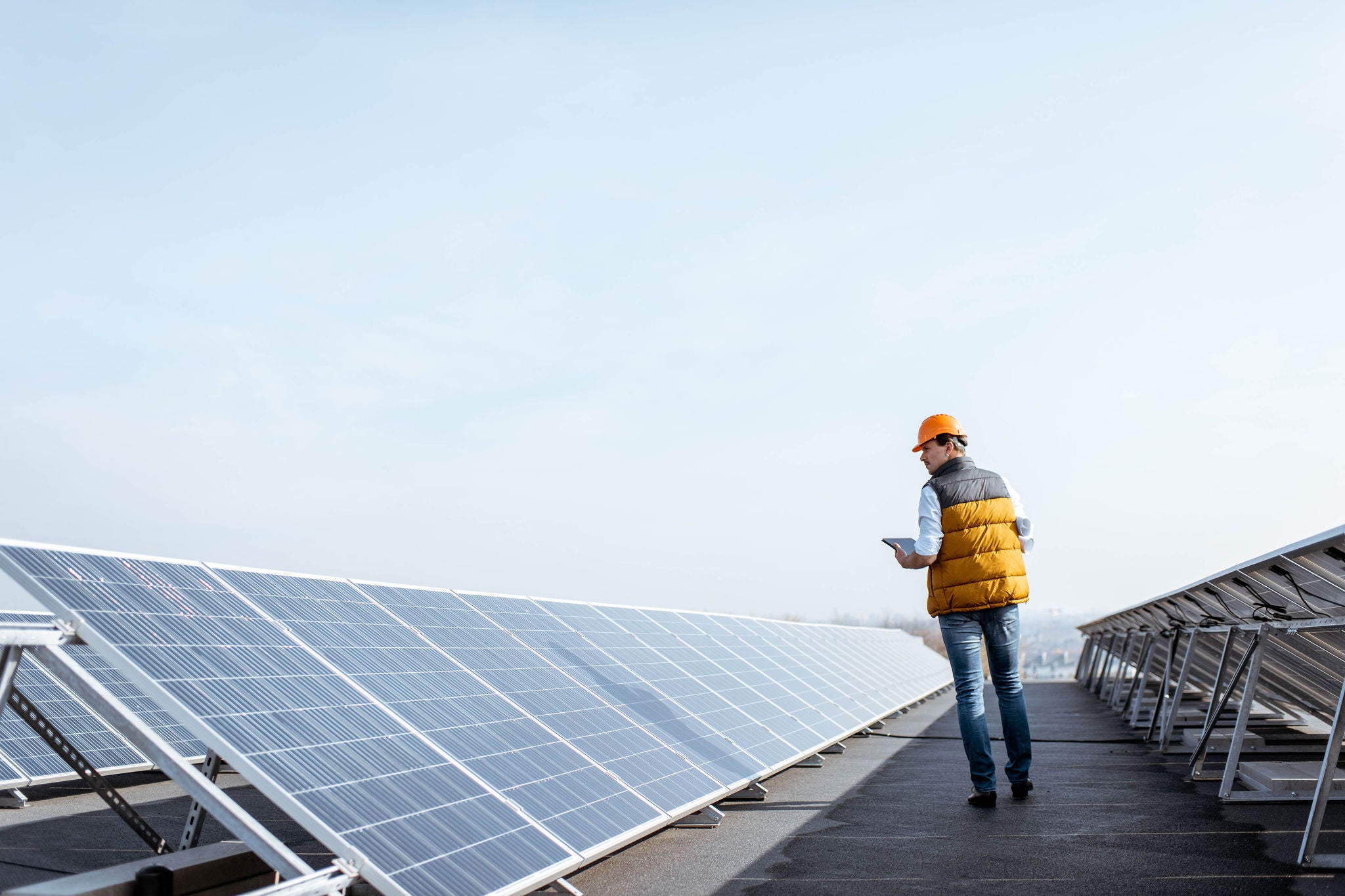 View on the rooftop solar power plant with mann walking and examining photovoltaic panels. Concept of alternative energy and its service
