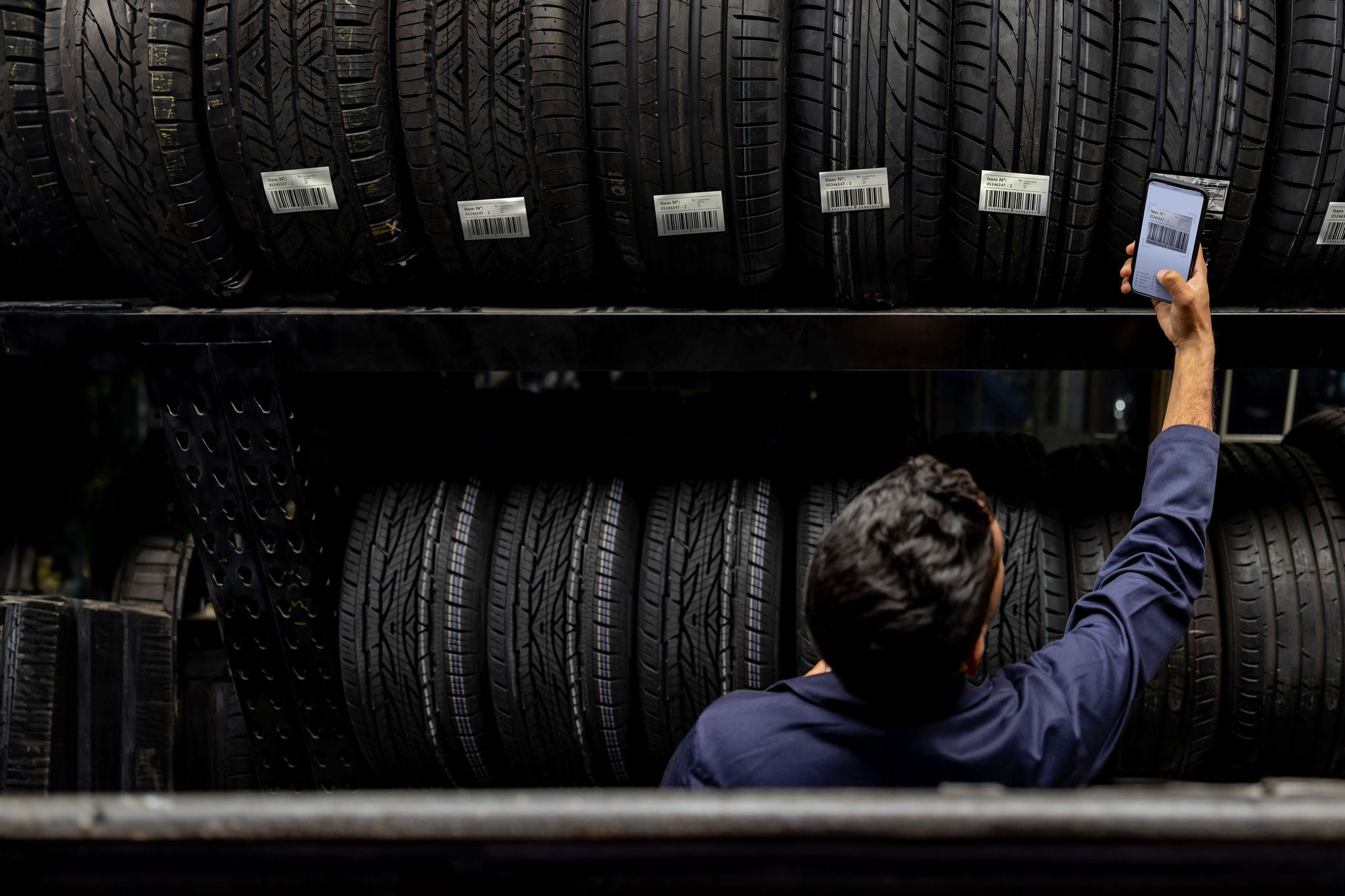 Latin American employee scanning a bar code on a tire at a garage shop using a cell phone