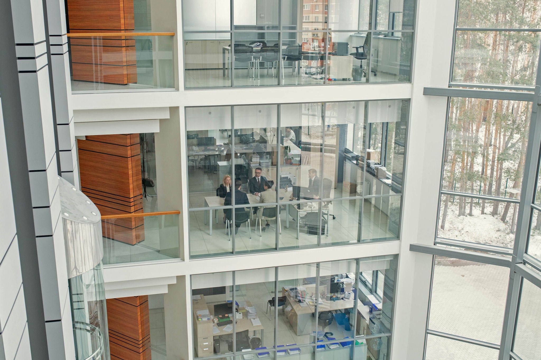 Image of modern office building with big windows and business people working together inside of it